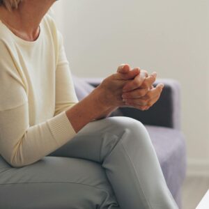 An elderly woman seated thoughtfully in an indoor counseling setting.